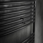 Pojedynczy haczyk na kaloryfer w kolorze czarny mat, na tle eleganckiej ciemnej łazienki, oraz kaloryfera drabinkowego