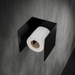 Czarny, metalowy uchwyt na papier toaletowy Nira, zamontowany na betonowej ścianie w nowoczesnej łazience – minimalistyczny design w stylu industrialnym