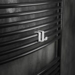 Podwójny haczyk na kaloryfer, aluminiowy, na tle eleganckiej łazienki oraz kaloryfera drabinkowego. W kolorze biały mat