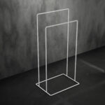 biały, minimalistyczny stojak łazienkowy na ręczniki AVRO ustawiony na ciemnej, betonowej podłodze przy ścianie z surowego betonu.