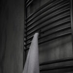 Pojedynczy haczyk na kaloryfer w kolorze czarny mat, na tle eleganckiej ciemnej łazienki, oraz kaloryfera