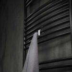 Pojedynczy haczyk na kaloryfer w kolorze biały mat, na tle eleganckiej ciemnej łazienki, oraz kaloryfera