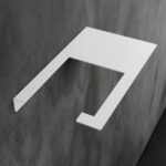 Minimalistyczny uchwyt na papier toaletowy Sora w kolorze matowej bieli, wykonany z jednego giętego elementu metalu, o nowoczesnej i geometrycznej formie – widok z ukosa na tle łazienki