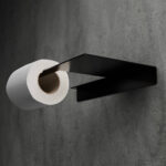 Minimalistyczny uchwyt na papier toaletowy Sora w kolorze matowej czerni, wykonany z jednego giętego elementu metalu, o nowoczesnej i geometrycznej formie – widok z ukosa na tle łazienki