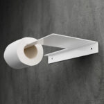 Minimalistyczny uchwyt na papier toaletowy Sora w kolorze matowej bieli, wykonany z jednego giętego elementu metalu, o nowoczesnej i geometrycznej formie – widok z ukosa na tle łazienki