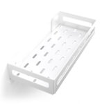 Biała metalowa półka łazienkowa NAOS z matowym wykończeniem, zamontowana na ścianie, z perforowanym dnem i wysokimi bokami; na półce ustawione butelki kosmetyków.