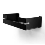 Czarna, metalowa półka łazienkowa VEGA z matowym wykończeniem, zamontowana na ścianie, z widocznymi kroplami wody. Na półce ustawione są eleganckie kosmetyki w ciemnych butelkach. Konstrukcja posiada perforowane dno dla odpływu wody oraz wysokie boki zabezpieczające przed zsuwaniem się przedmiotów.