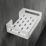 Biała metalowa półka łazienkowa NAOS z matowym wykończeniem, zamontowana na ścianie, z perforowanym dnem i wysokimi bokami; na półce ustawione butelki kosmetyków.