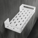 Biała metalowa półka łazienkowa NAOS z matowym wykończeniem, zamontowana na ścianie, z perforowanym dnem i wysokimi bokami; na półce ustawione butelki kosmetyków.