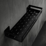 Czarna metalowa półka łazienkowa NAOS z matowym wykończeniem, zamontowana na ścianie, z perforowanym dnem i wysokimi bokami; na półce ustawione butelki kosmetyków.