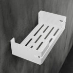 Biała, metalowa półka łazienkowa VEGA z matowym wykończeniem, zamontowana na ścianie, z widocznymi kroplami wody. Na półce ustawione są eleganckie kosmetyki w ciemnych butelkach. Konstrukcja posiada perforowane dno dla odpływu wody oraz wysokie boki zabezpieczające przed zsuwaniem się przedmiotów.